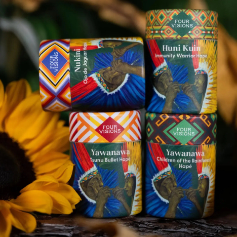 Four Visions Hap&eacute; containers stacked beside yellow sunflowers, featuring colorful geometric packaging for Yawanawa, Nukini, and Huni Kuin blends.
